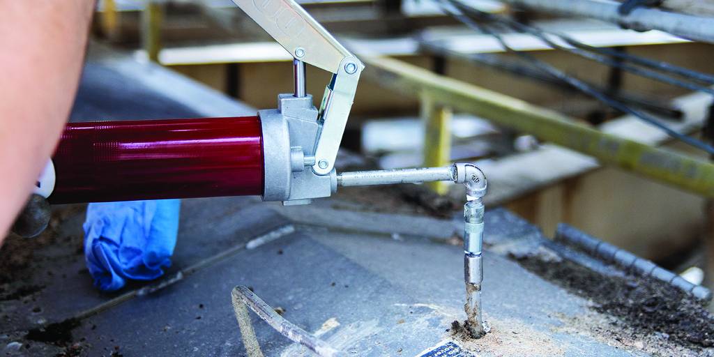 Grease gun applying lubricant to industrial equipment